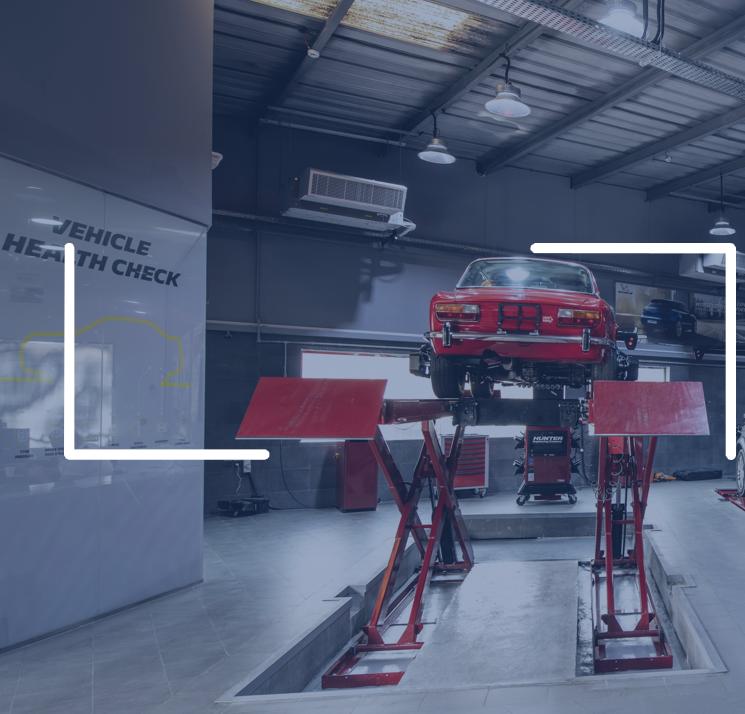 A car raised on a lift beside a Vehicle Health Check display board.